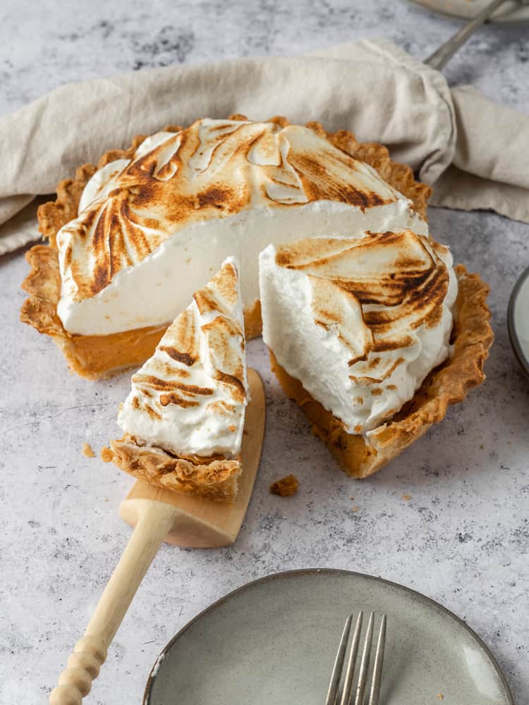 A pumpkin meringue pie with a slice being pulled out of it