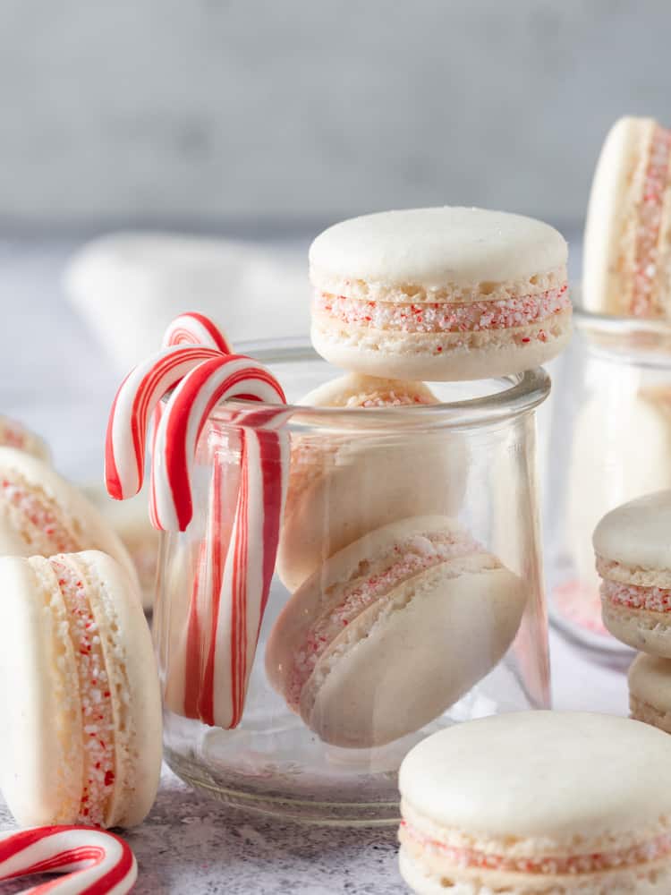A small glass jar with candy canes on the side and peppermint macarons inside