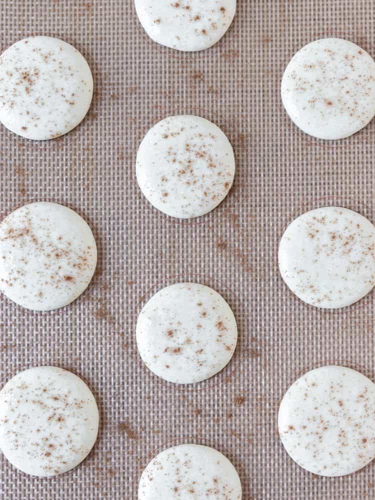 cinnamon roll macarons piped onto a baking sheet