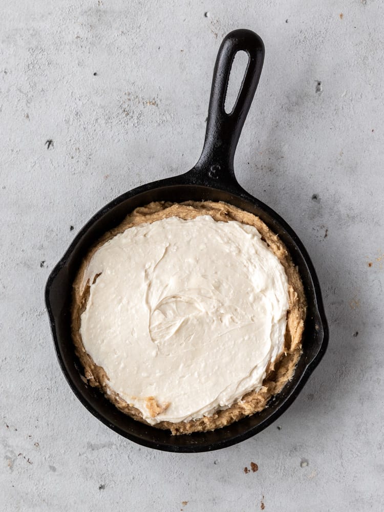 Half of the cookie dough pressed into the skillet with the cheesecake filling spread on top
