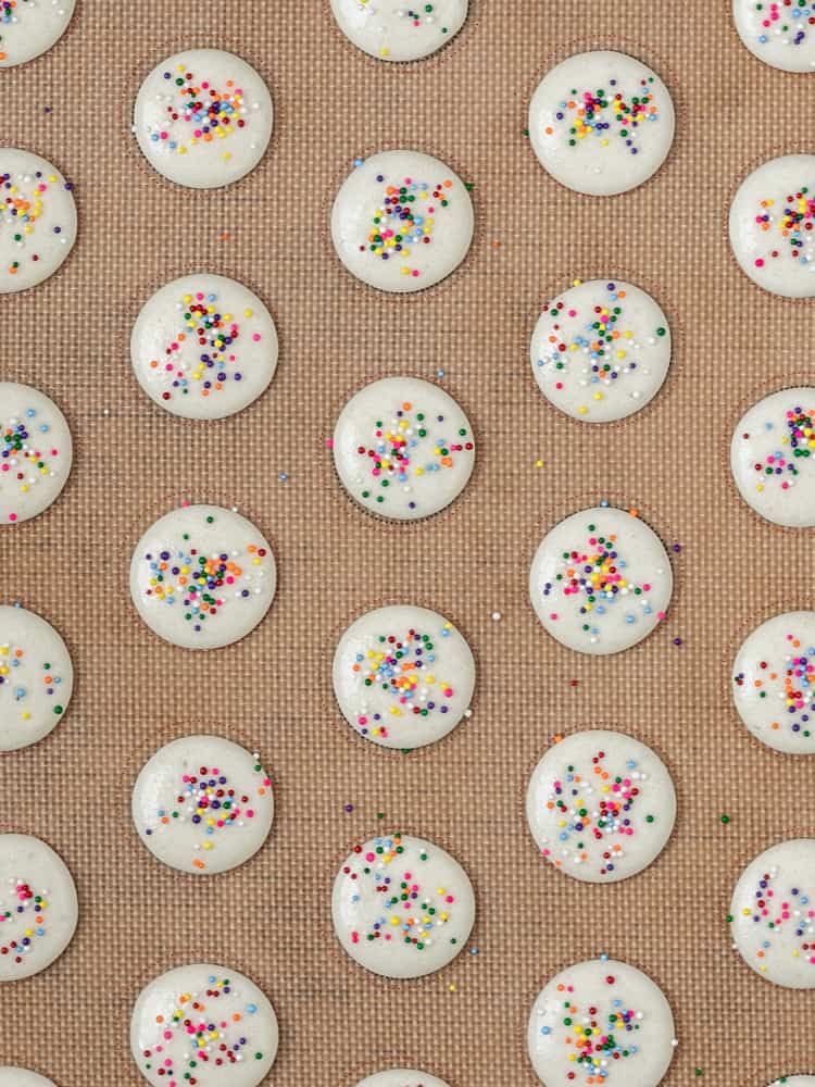 The macarons piped on a baking sheet and topped with sprinkles