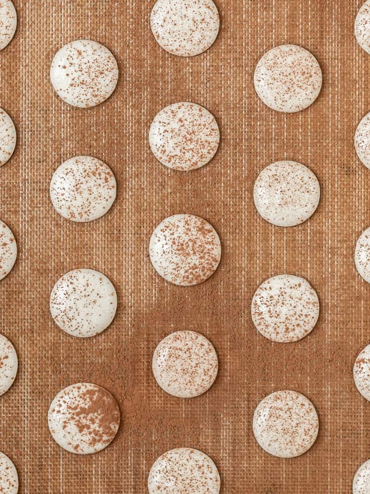 The macarons piped onto a baking sheet and dusted with cocoa powder