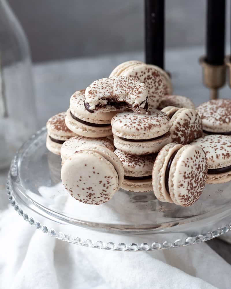 A side view of a stack of chocolate macarons, one has a bite out of it
