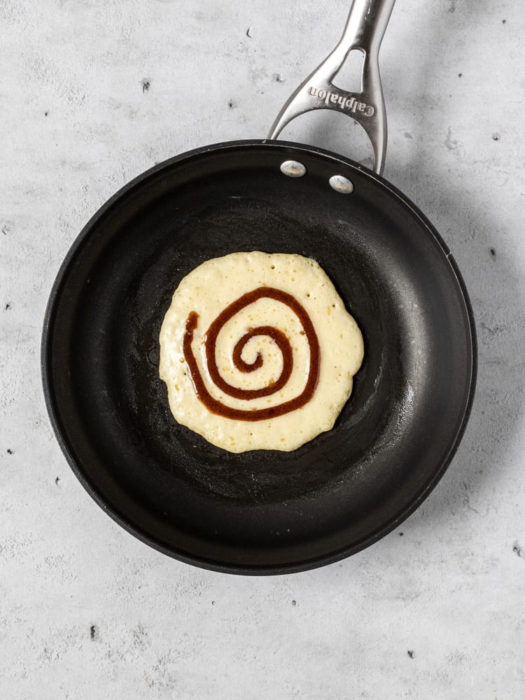 A pancake in a pan with the cinnamon swirl piped on top