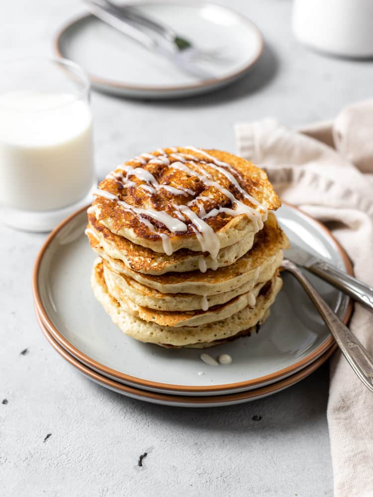 Cinnamon swirl pancakes stacked on a plate and drizzled with cream cheese icing. 