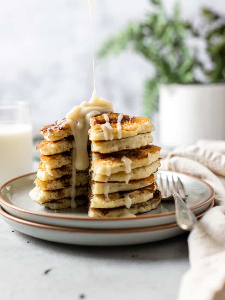 A stack of cinnamon swirl pancakes being drizzled with cream cheese icing.