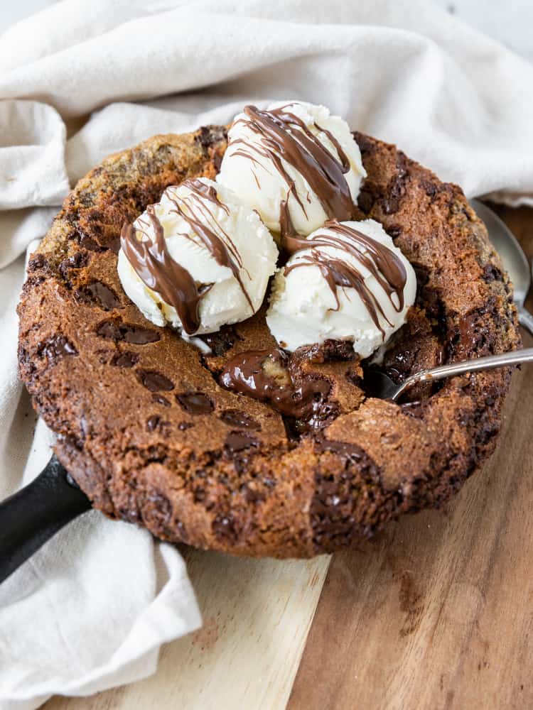 A skillet cookie with a gooey center that is topped with ice cream