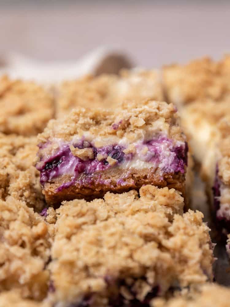 A blueberry crumble cheesecake bar propped up on other bars