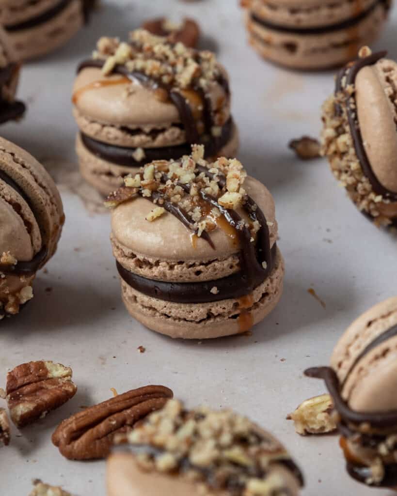 A closeup of a french macaron drizzled with chocolate ganache, caramel, and pecans