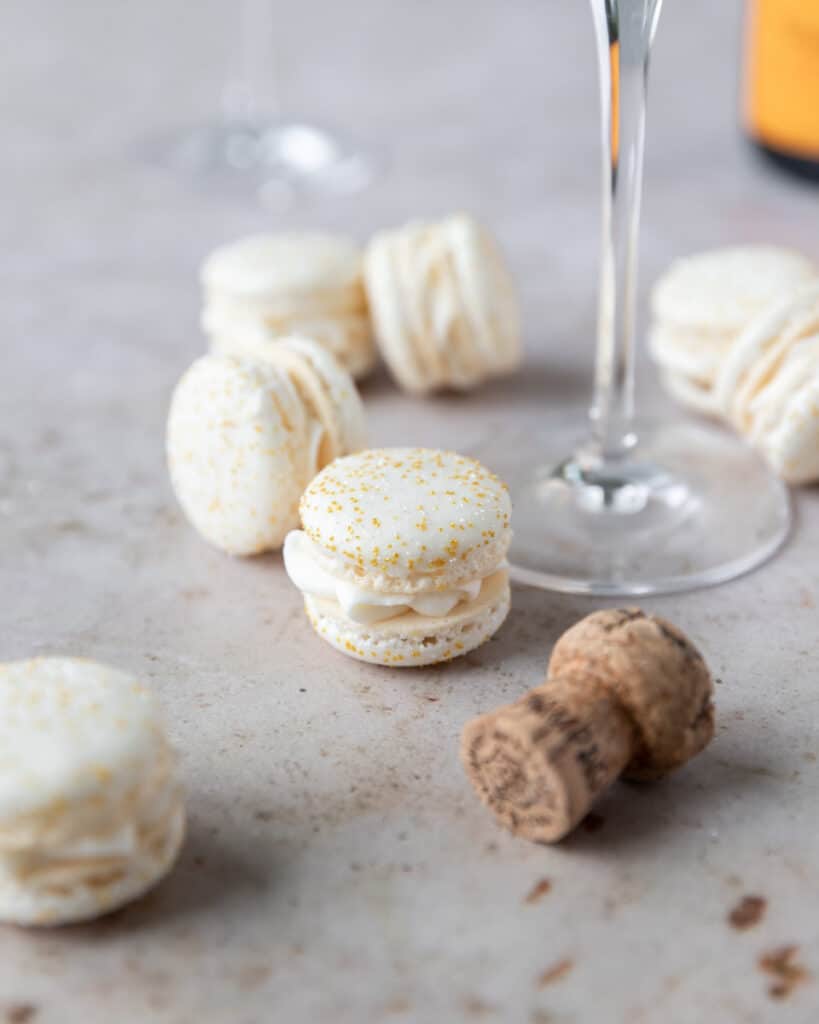 a french macaron filled with champagne buttercream sitting beside a champagne glass