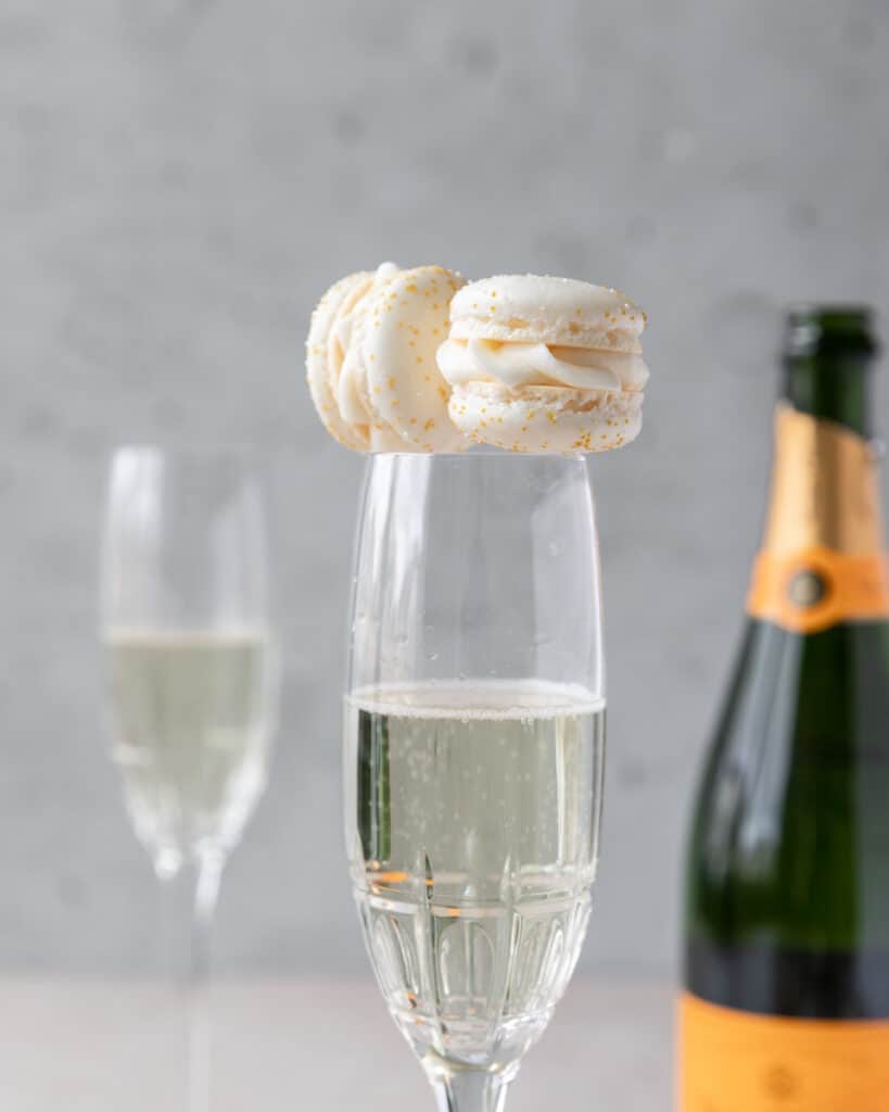 two french macarons sitting on top of a glass of champagne