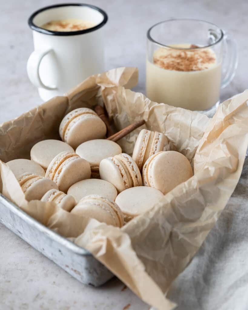Egg nog macarons in a dish next to two glasses of egg nog