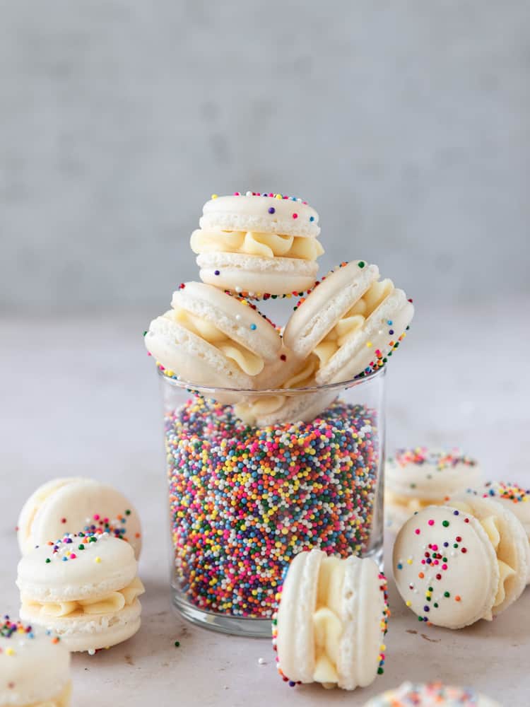 birthday cake macarons stacked on a cup full of sprinkles