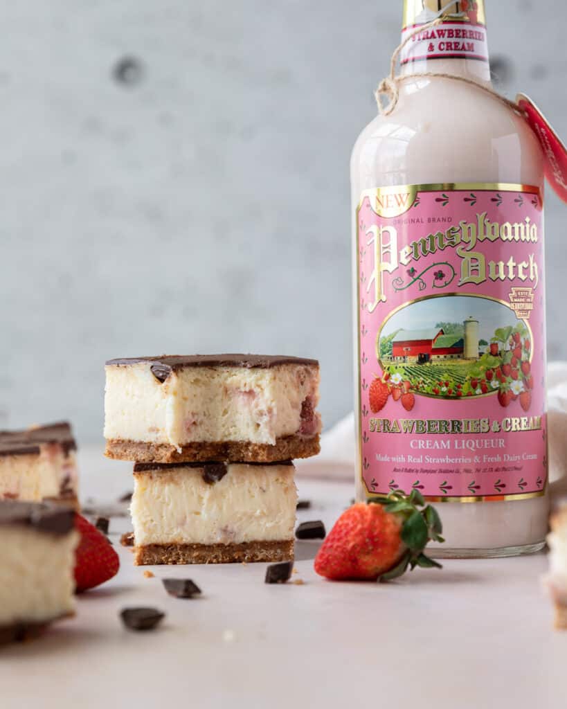two strawberry cheesecake bars beside a bottle of Pennsylvania dutch strawberries and cream liqueur