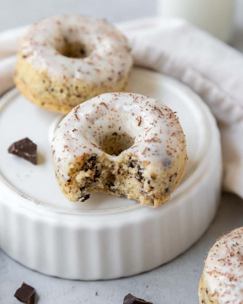 two chocolate chip donuts on an overturned dish. One has a bite out of it
