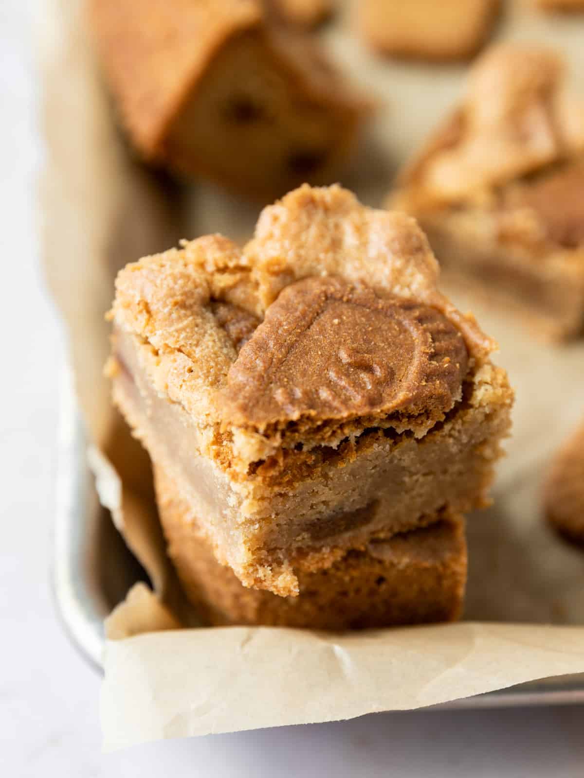 two biscoff blondies stacked on top of each other and set on the edge of a baking sheet