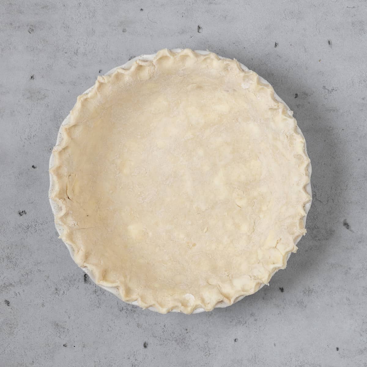 the pie dough pressed into a pie dish before being baked on a grey background
