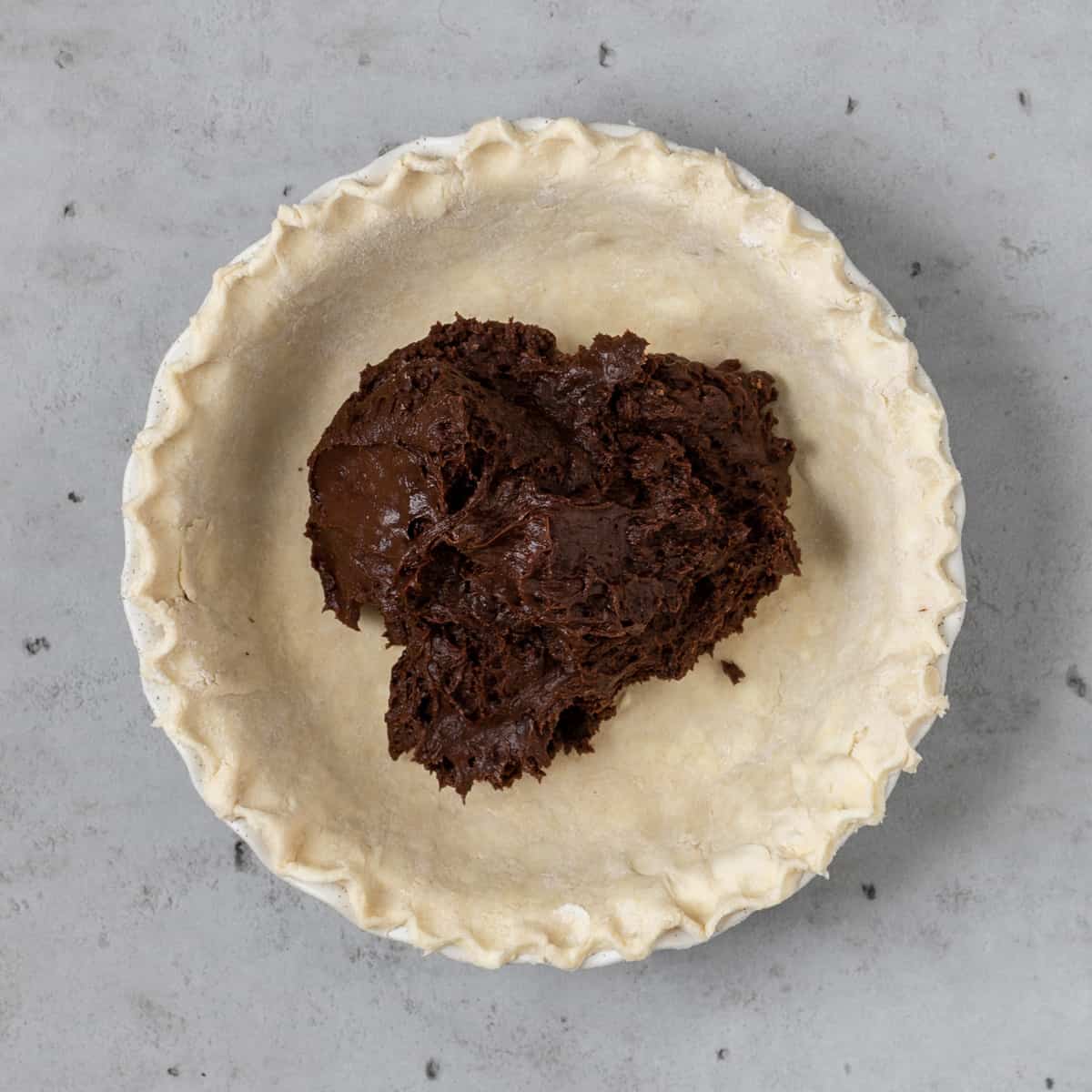 The brownie batter in the prepared pie dough before being baked on a grey background