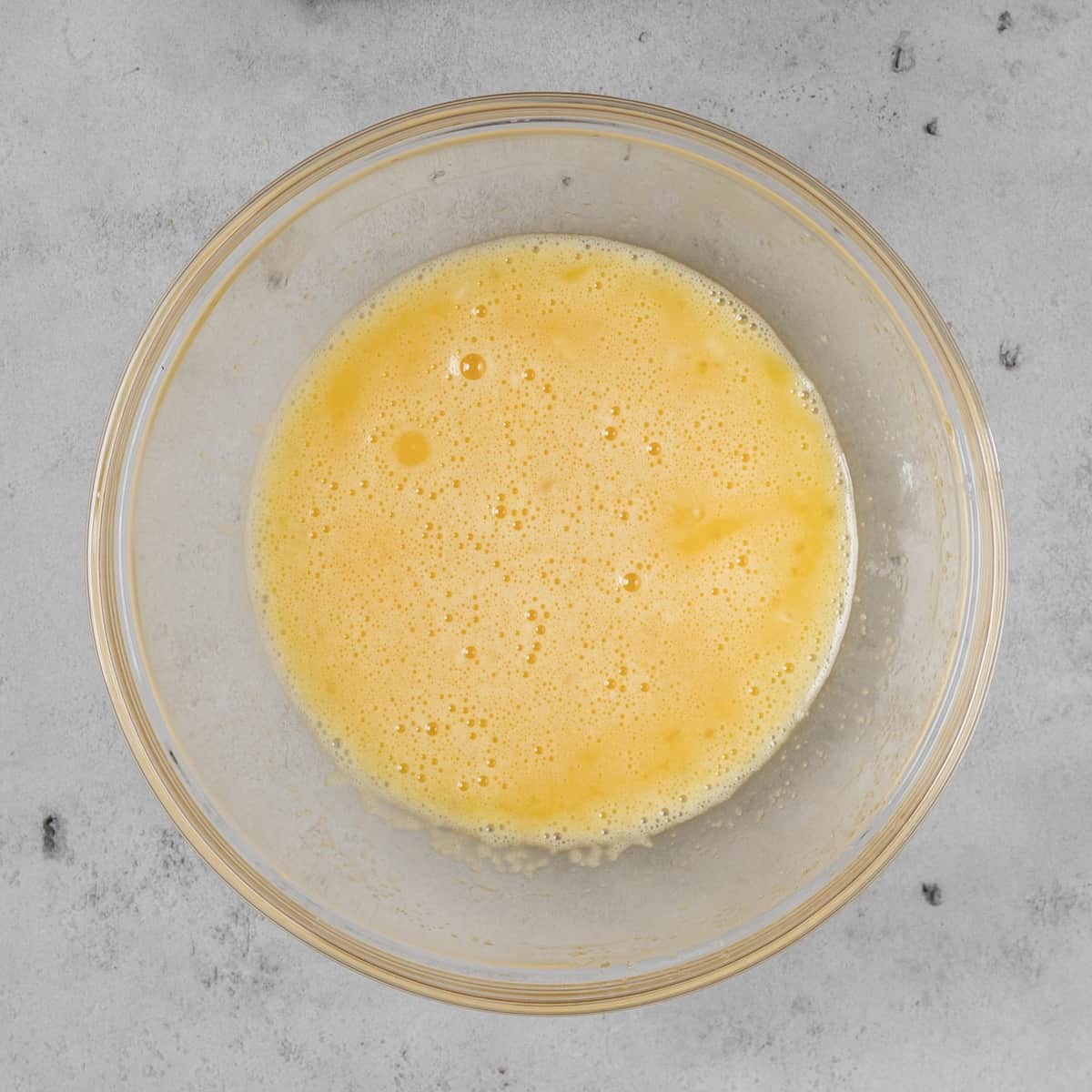 the eggs and sugar combined in a glass bowl on a grey background
