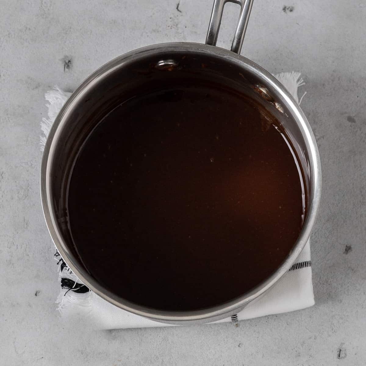 the butter and chocolate melted together in a small stainless steel saucepan on a grey background.