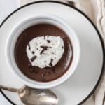 a closeup of a chocolate pots de crème in a ramekin topped with whipped cream and chocolate.