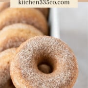 a close up of a cinnamon sugar donut balanced on the edge of a dish. It says cinnamon sugar donuts across the top