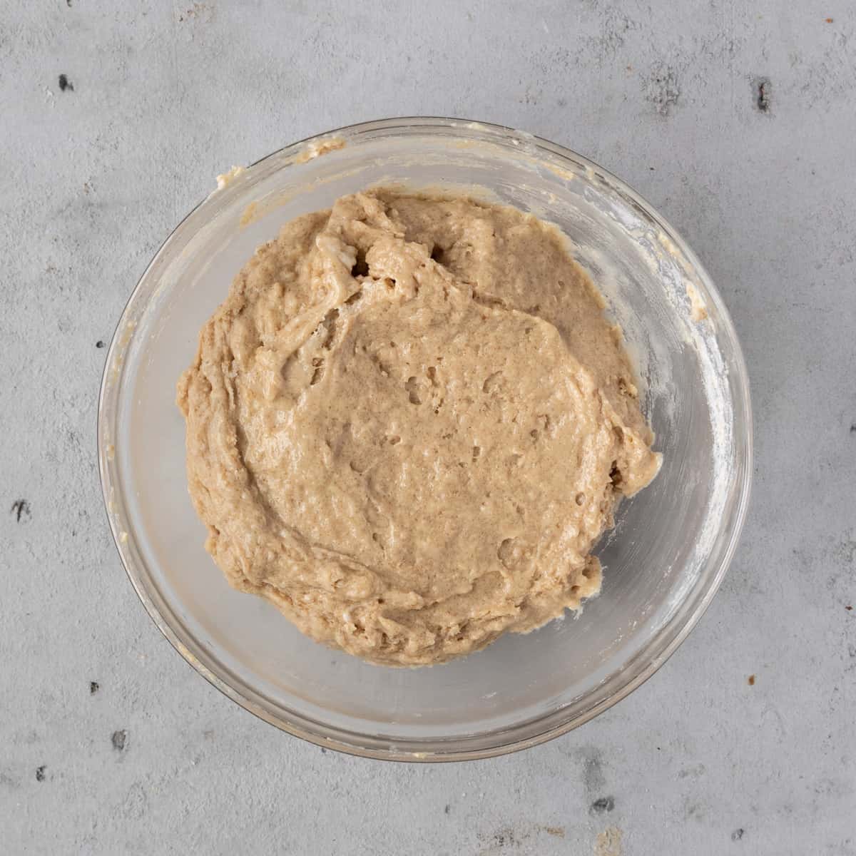 the wet and dry ingredients combined into the completed donut batter in a glass bowl on a grey background