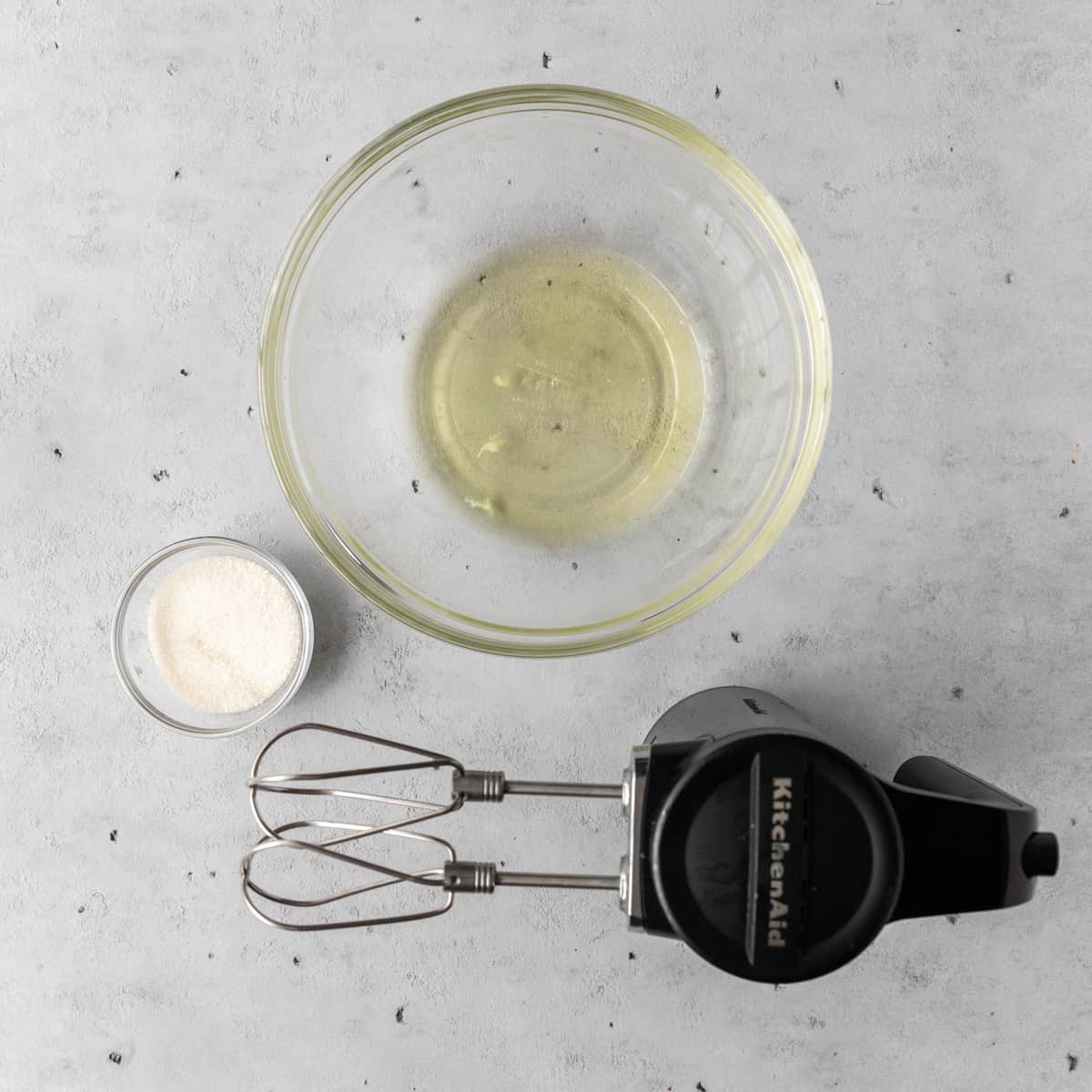 the egg whites, sugar, and hand mixer on a grey background