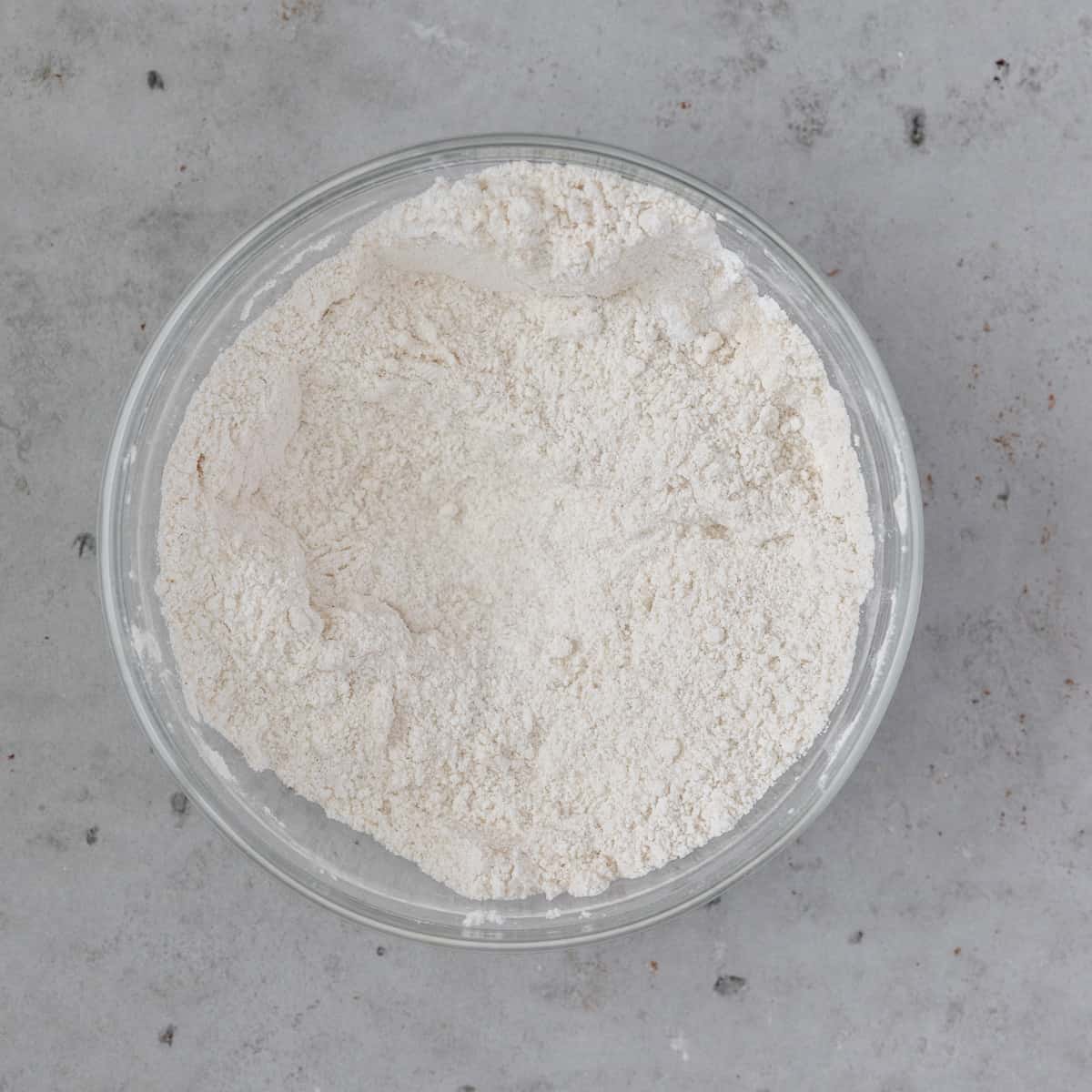 all of the dry ingredients combined in a glass bowl on a grey background