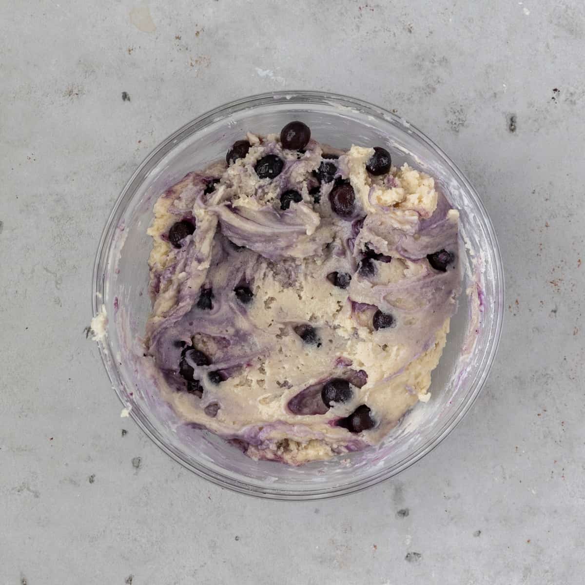 the completed gluten free blueberry muffin batter in a glass bowl on a grey background