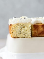a close-up shot of a slice of lemon poppy seed cake sitting on a cream colored dish