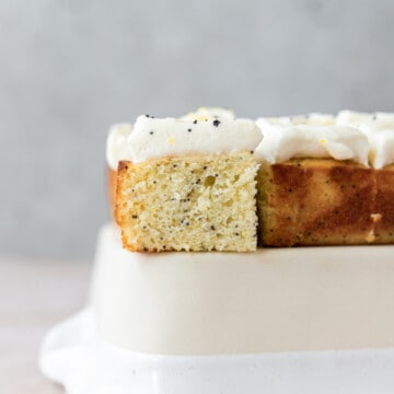 a close-up shot of a slice of lemon poppy seed cake sitting on a cream colored dish