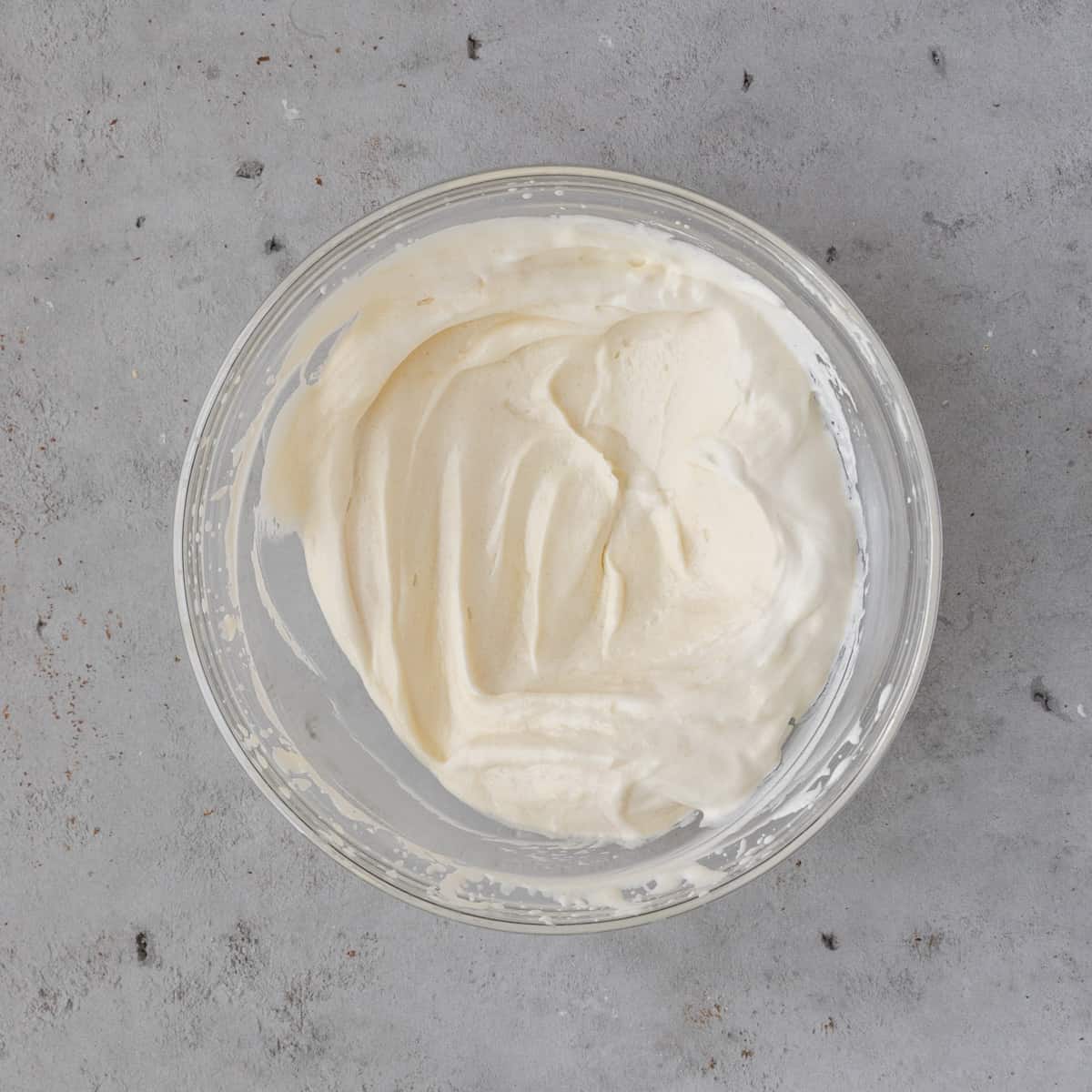 the whipped cream cheese icing in a glass bowl on a grey background