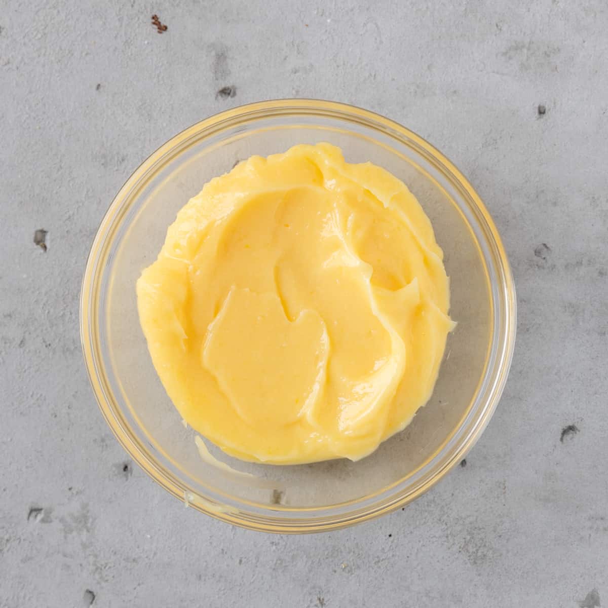 the lemon curd in a glass bowl on a grey background.