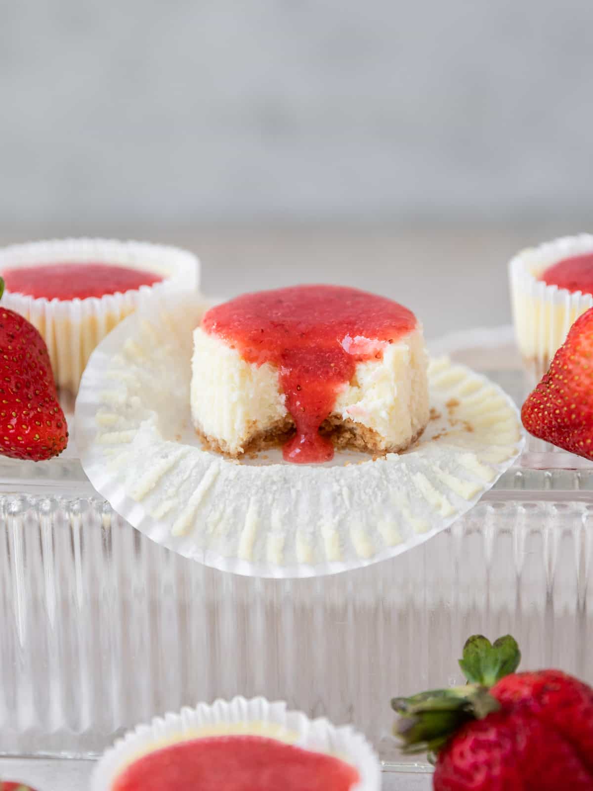 a mini strawberry cheesecake with a bite out of it with strawberry sauce dripping down the front