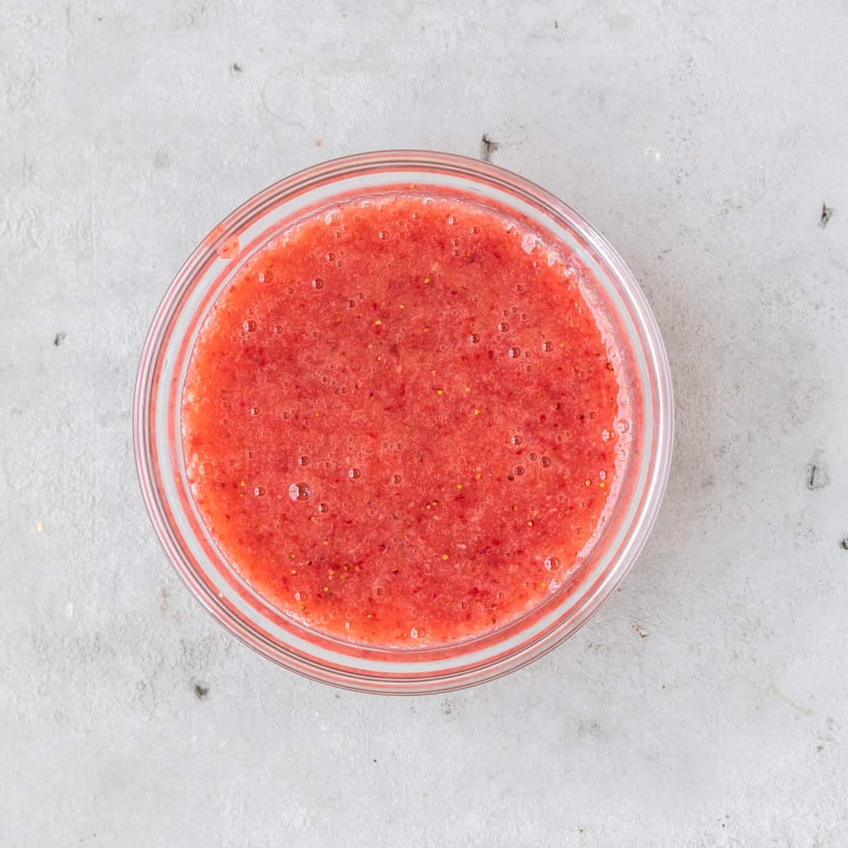 the strawberry sauce in a glass bowl on a grey background