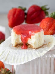 a mini strawberry cheesecake with a bite out of it surrounded by fresh strawberries on a glass dish