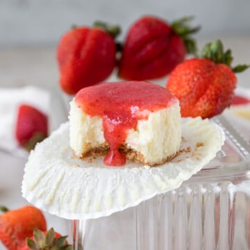 a mini strawberry cheesecake with a bite out of it surrounded by fresh strawberries on a glass dish