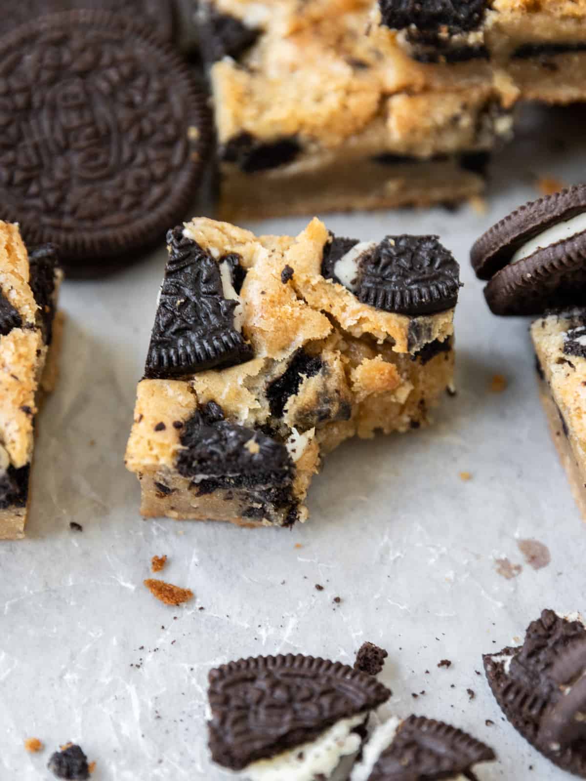 a close up of an oreo bar with a bite out of it on a white background surrounded by other bars and crushed up oreos