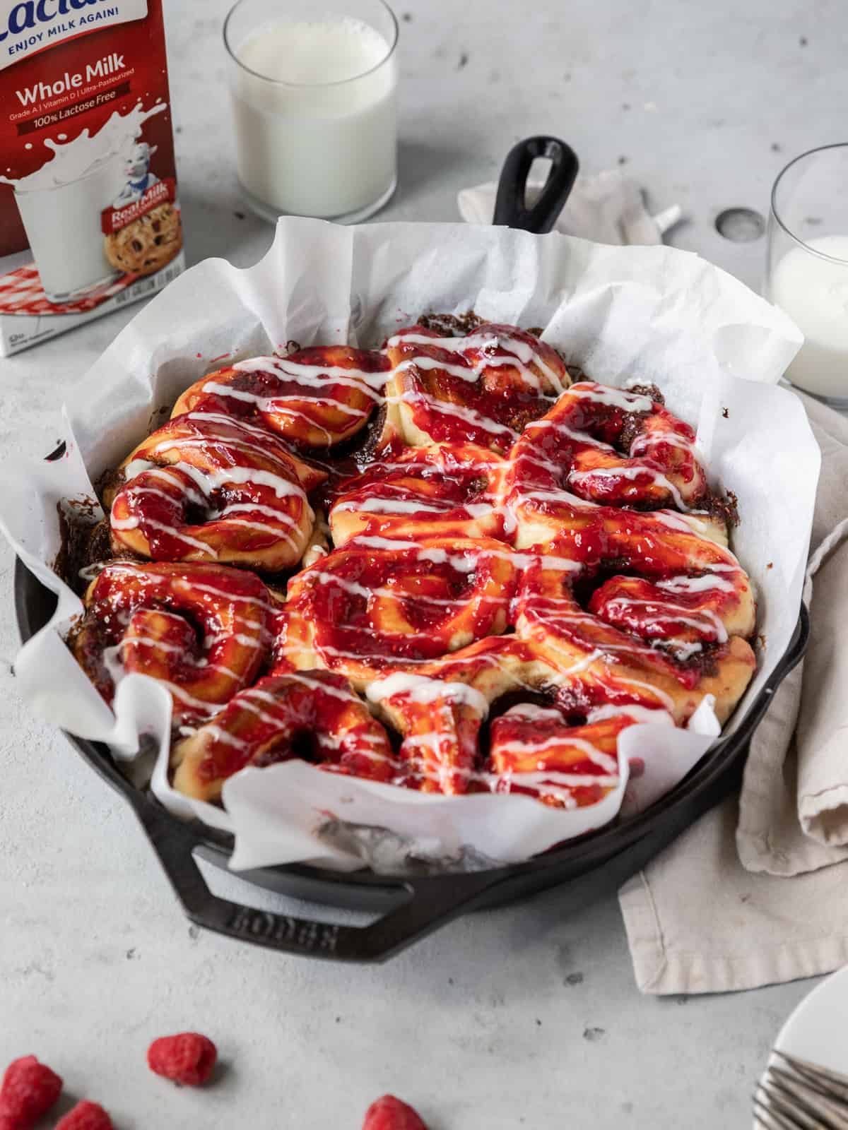 raspberry cinnamon rolls in a cast iron dish with two glasses of milk behind it