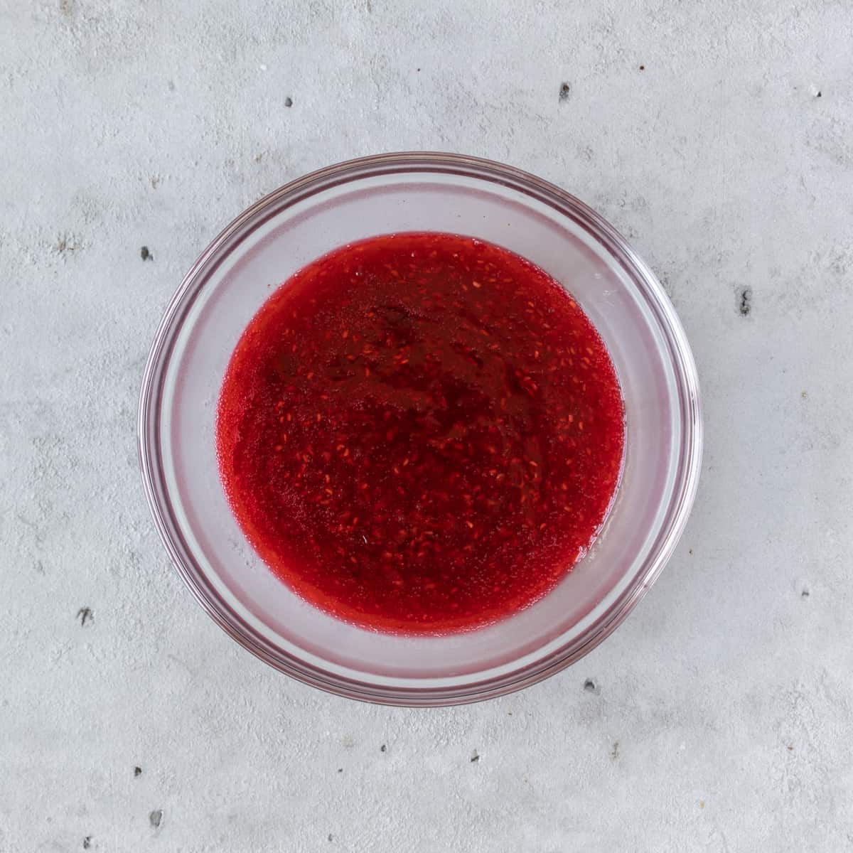 the raspberry jam in a glass bowl on a grey background