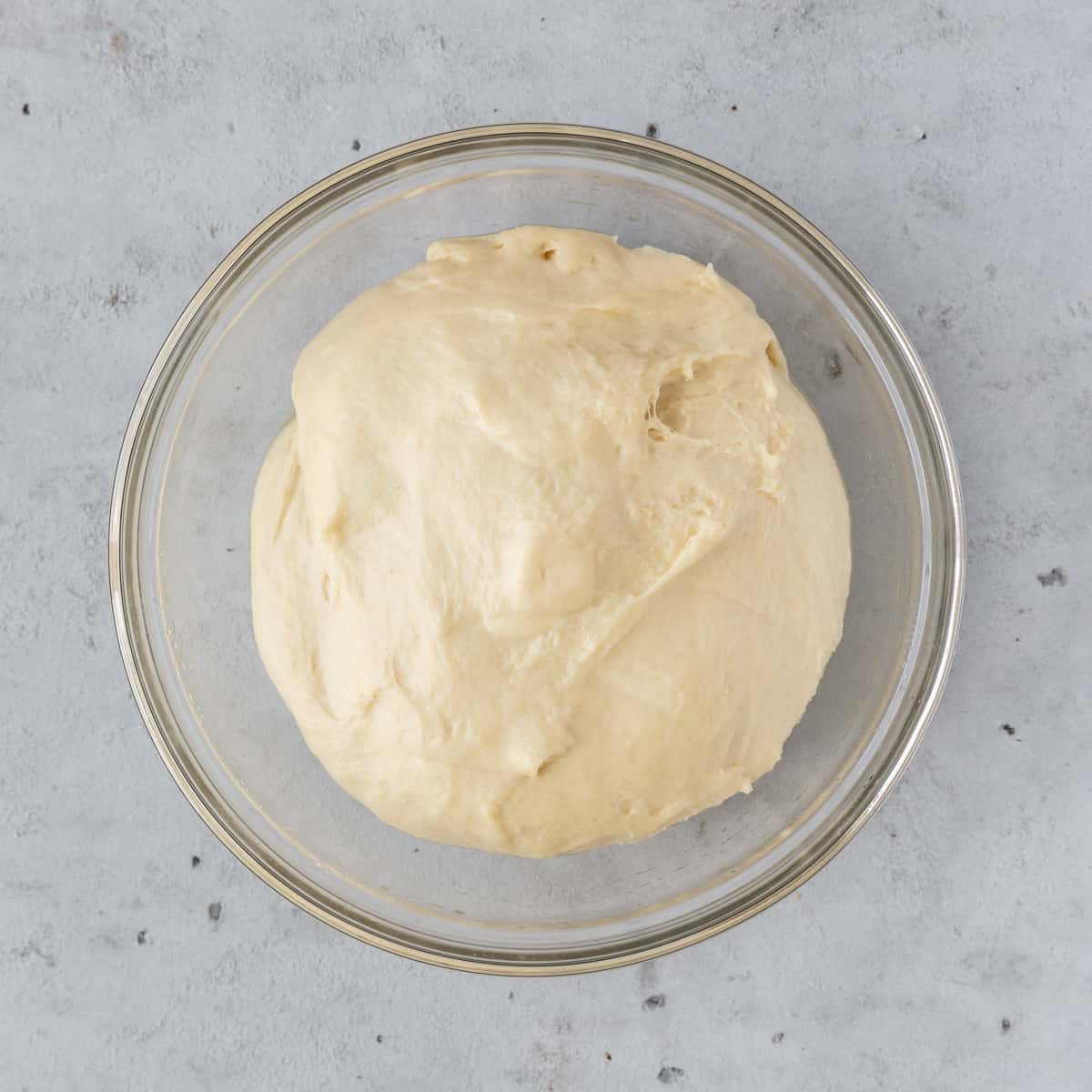 the risen dough in a glass bowl on a grey background