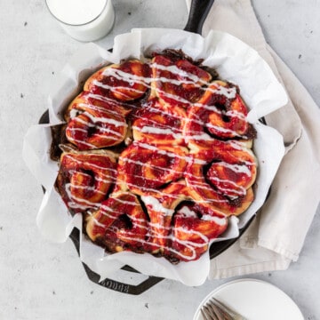 looking down on a cast iron dish full of raspberry cinnamon rolls on a grey background