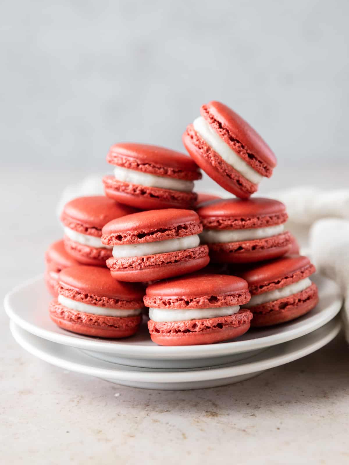 a tower of red velvet macarons on a white plate on a tan background