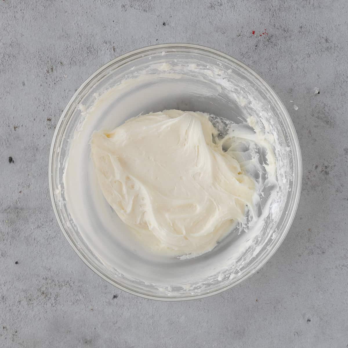 the cream cheese buttercream in a glass bowl on a grey background