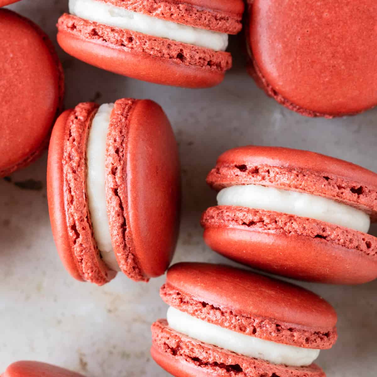 a close up of several red velvet macarons on a tan background