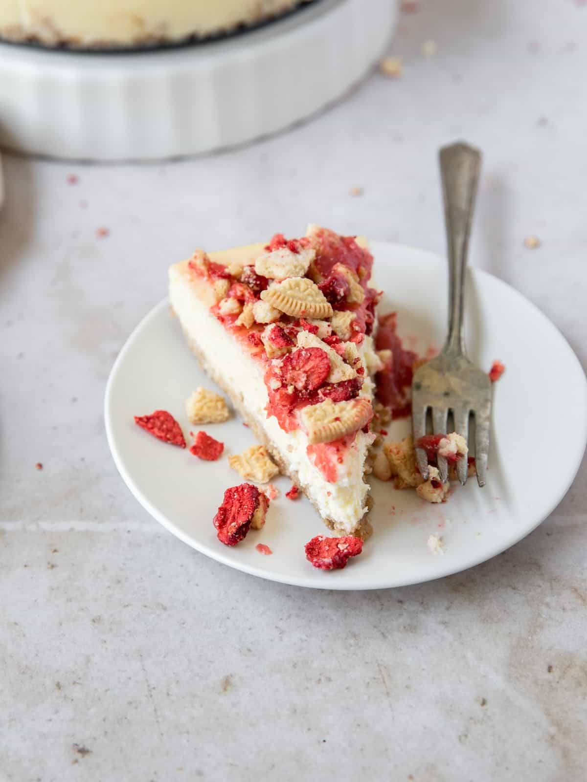 a slice of strawberry crunch cheesecake on a white plate with a fork next to it