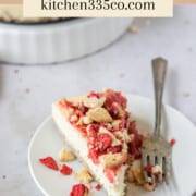 a slice of strawberry crunch cheesecake on a white plate with a fork next to it. it says strawberry crunch cheesecake across the top.