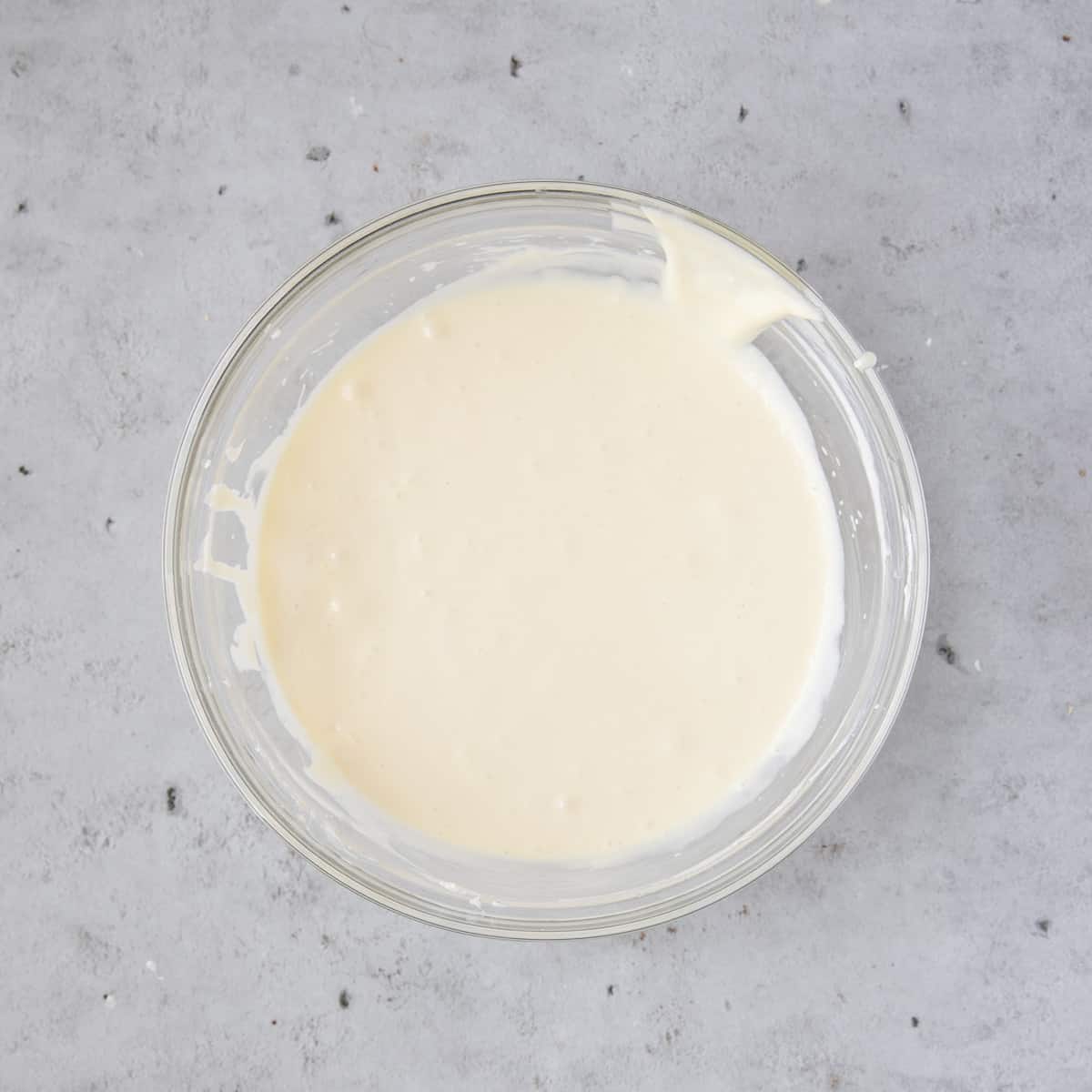 the cheesecake filling in a glass bowl on a grey background