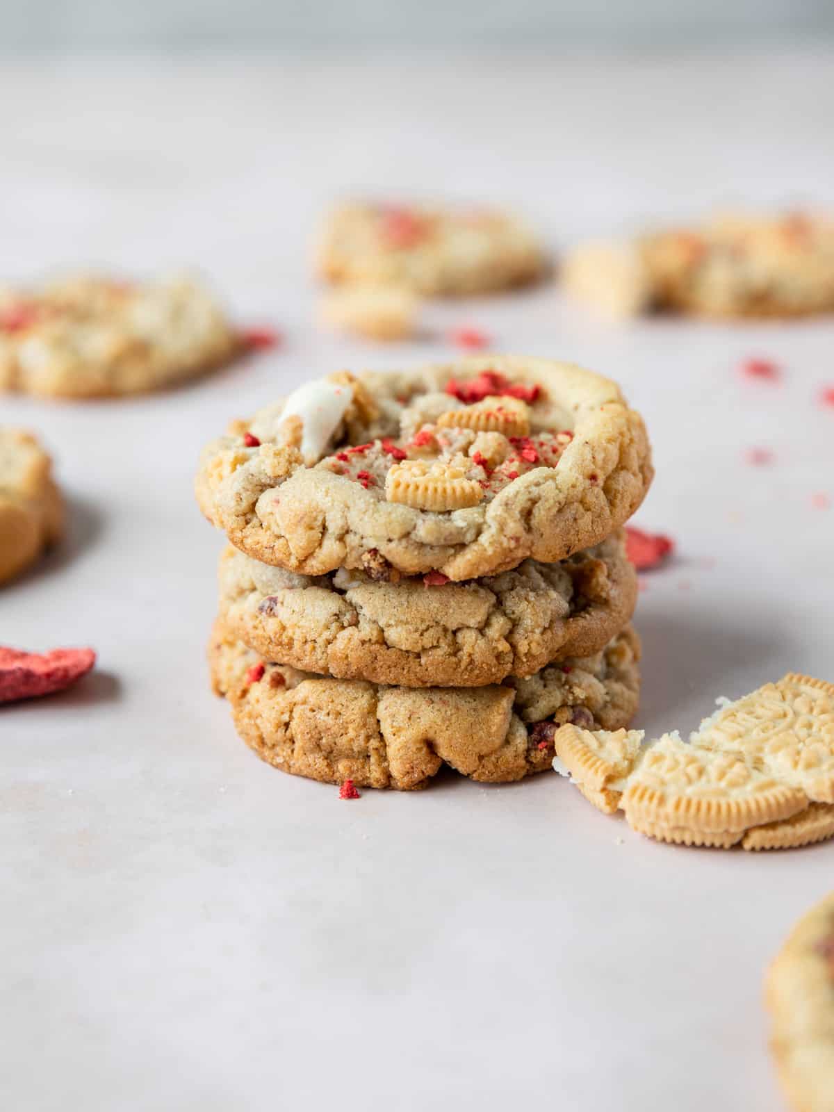 a stack of three strawberry crunch cookies surrounded by freeze dried strawberries and crushed up golden oreos